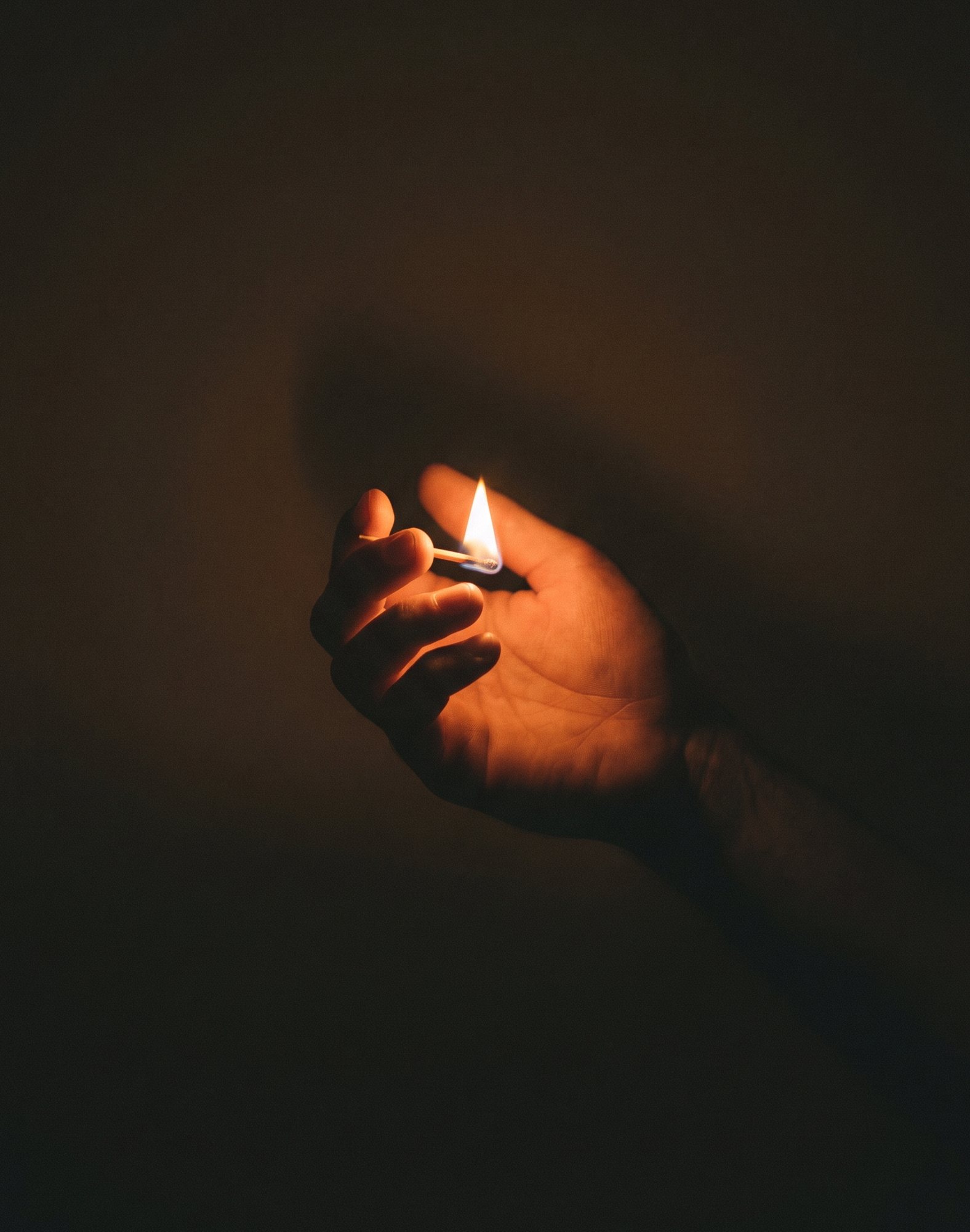A match held in a hand, its flame lighting the surrounding darkness.